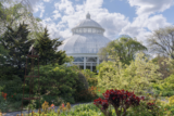A white conservatory dome rises over a sunny green garden space